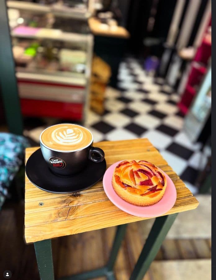 Cafea cu lapte și o tartă cu prune pe o măsuță de lemn, cu podeaua în carouri în fundal
